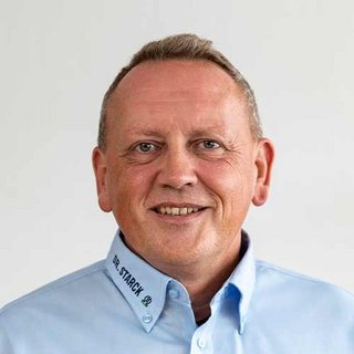 Ein lächelnder Mann mit kurzen, grauen Haaren trägt ein hellblaues Hemd mit dem Aufdruck 'DR. STARCK'.