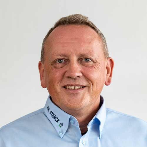 Ein lächelnder Mann mit kurzen, grauen Haaren trägt ein hellblaues Hemd mit dem Aufdruck 'DR. STARCK'.