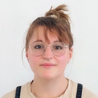 Eine junge Frau mit Brille und einem lässigen Outfit blickt freundlich in die Kamera, ihre Haare sind locker hochgesteckt.