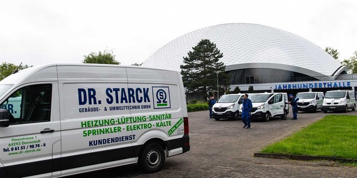 Ein moderner Lieferwagen mit dem Logo von Dr. Starck steht vor der Jahrhunderthalle, umgeben von weiteren Fahrzeugen.