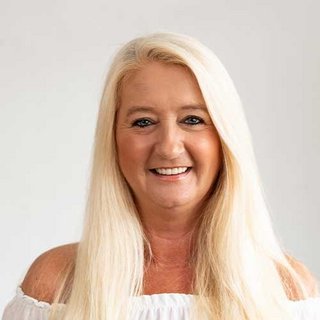 Die Frau trägt ein offenes, weißes Oberteil und strahlt Freude aus, während sie direkt in die Kamera schaut.