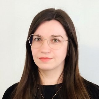 Eine junge Frau mit langen, glatten Haaren und einer neutralen Miene trägt modische Brillen und ein schwarzes Oberteil.