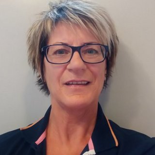 Eine Frau mit kurzen, blonden Haaren und Brille lächelt freundlich in die Kamera, vor einem neutralen Hintergrund.